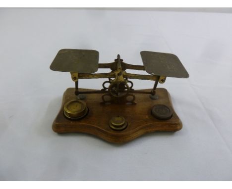 A set of brass postal scales with weights on shaped rectangular oak base