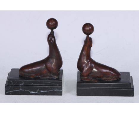 A pair of Art Deco design brown patinated bronze bookends, each cast with a seal balancing a ball, stepped marble bases, 15cm