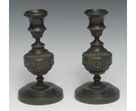 A pair of Regency brown patinated bronze candlesticks, campana sconces, each with fluted knop centred by a band of leafy Vitr