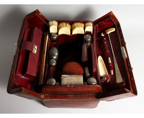 A GENTLEMAN'S CROCODILE TRAVELLING CASE with silver and ivory fittings, seven silver top bottles, watch case, shaving case pl