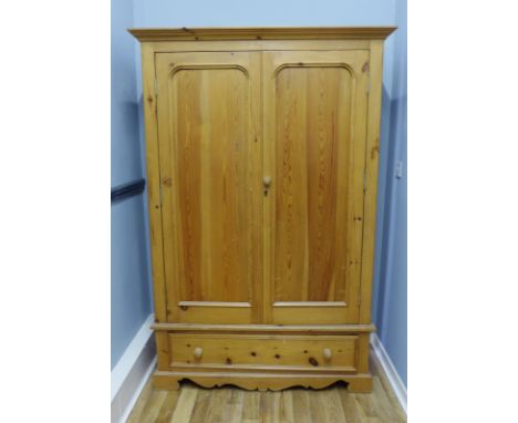 A contemporary pine two door wardrobe having a moulded cornice to top above two panel doors and one long drawer raised on bra