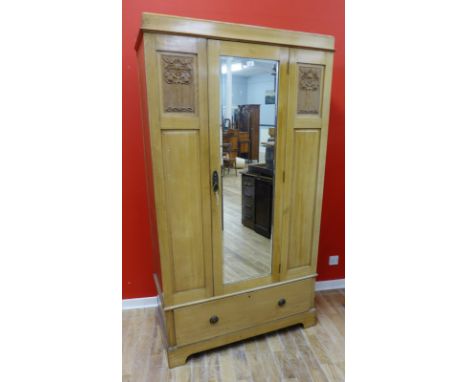 An Arts & Crafts pine mirrored door wardrobe with moulded cornice above mirrored panel door enclosing fitted interior over on
