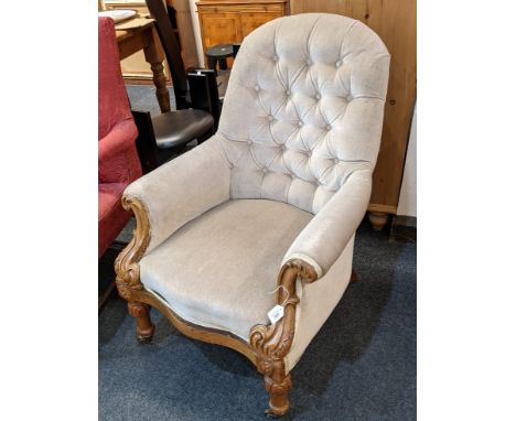 A Victorian button back upholstered armchair, with carved arm supports and legs, on castors