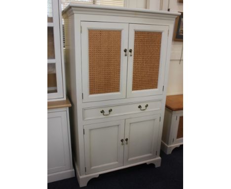 A Laura Ashley cream painted tall cupboard, with two wicker front panel doors enclosing shelf, above a drawer with further cu