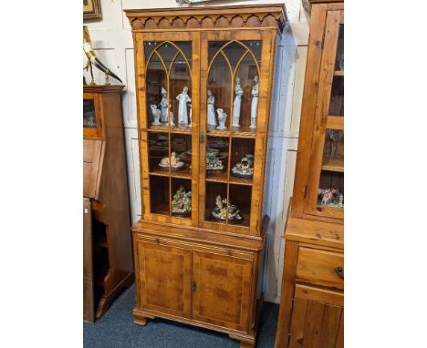 A yew wood veneered bookcase, with two glazed panel doors enclosing three adjustable shelves, above pull-out slide and cupboa