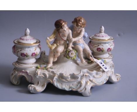 A SITZENDORF DESK TOP INKWELL, having figural seated cherubs flanked by floral decorated wells and covers with liners over sh