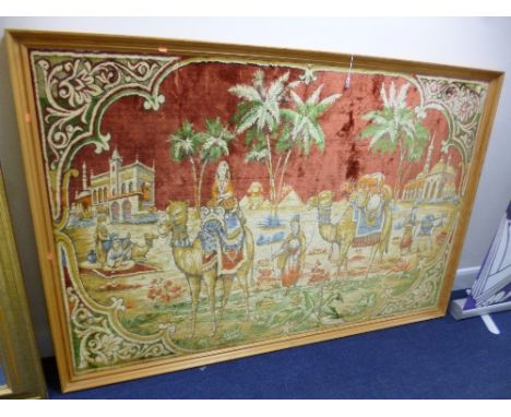 A LARGE WOVEN CARPET STYLE PICTURE, Camels with figures and buildings, approximate size including frame width 184cm x height 