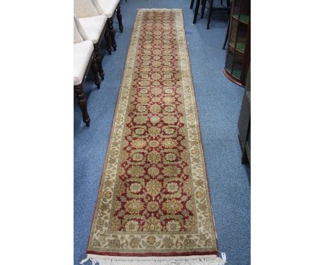 AN OLIVE GREEN AND RED GROUND CARPET RUNNER, 100% wool pile, hand knotted in India, approximate size 420cm x 70cm, G H Frith 