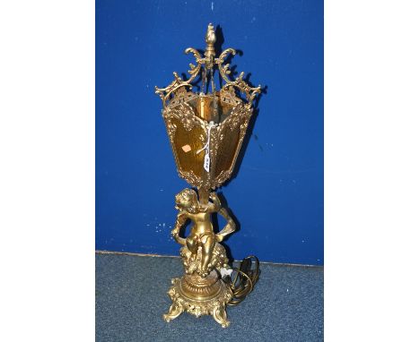 A FIGURAL TABLE LAMP, modelled as seated gilt cherub atop vines on scrolled base supporting lantern with amber shade, approxi