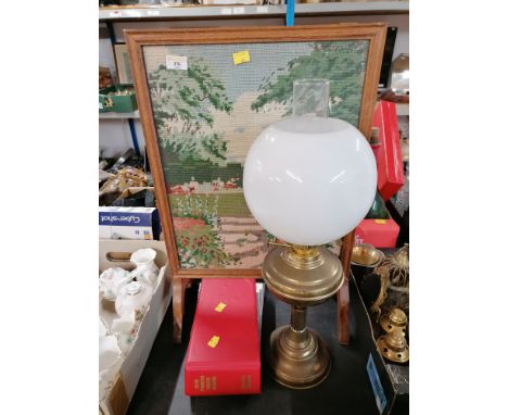 A brass oil lamp with glass shade, a needlework fire screen, and an album of first day covers  