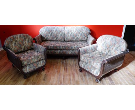 A three piece Edwardian hardwood Bergere suite to include a three seater sofa and two easy chairs having a carved hardwood fr