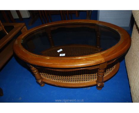 An oval glass top hardwood coffee table with pierced cane under shelf , 41" x 28" x 16"