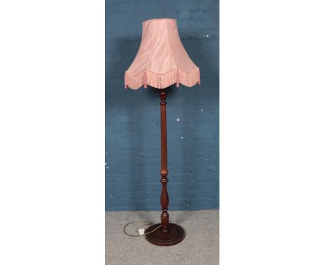 A turned mahogany standard lamp with pink fringed shade and circular base.  