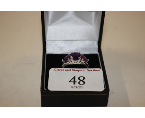 A white metal ring set three amethyst coloured stones