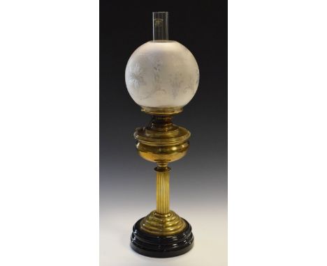 Early 20th Century brass oil lamp standing on a reeded pillar, black glazed ceramic base, together with a globular engraved f