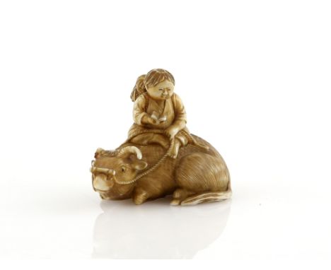 A stained ivory netsuke of a boy reading a text on the back of  recumbent water buffalo, 20th CenturyProvenance: The Property