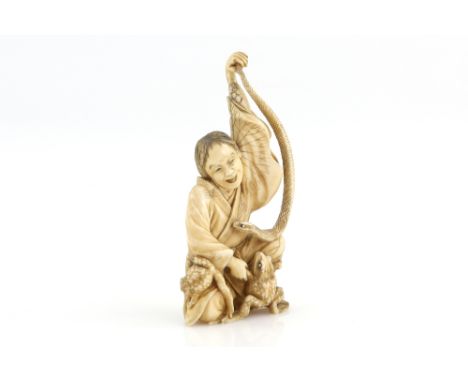 A stained ivory okimono, carved as a seated Sennin holding up a snake with the left hand; a frog beside him, 12 cm high, 19th