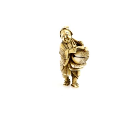 A stained ivory netsuke of a standing man beating a mokugyo, 19th  or 20th CenturyProvenance: The Property of a Lady. From a 