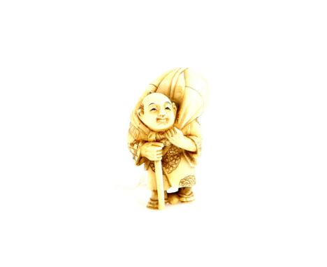 A stained ivory netsuke of a traveller wearing waraji, carrying a stick and holding a large sack over his right shoulder, 20t