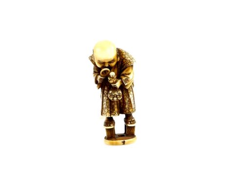 An ivory netsuke carved as a man wearing very tall geta whilst examining a netsuke with a magnifying glass,  20th CenturyProv