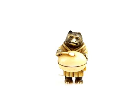 A stained ivory netsuke carved as a Tanuki bear banging a large mokugyo, 19th or 20th CenturyProvenance: The Property of a La