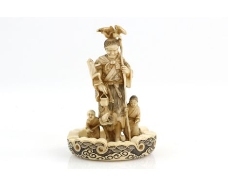 A stained ivory okimono carved as Gama Sennin, holding a staff in his left hand and flanked by two children and four jumping 