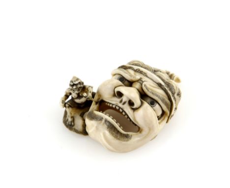 A stained ivory netsuke carved as an Oni using a chisel to sculpt a large mask of Emma-O, 20th CenturyProvenance: The Propert