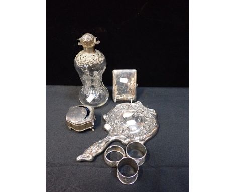 A SILVER MOUNTED DECANTER with other silver items including a cigarette case, a trinket box, three napkin rings and a white m