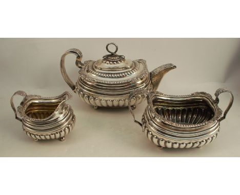 A Georgian silver three piece tea set, the tea pot with serpent finial, bands of gadrooned decoration and embossed shells to 