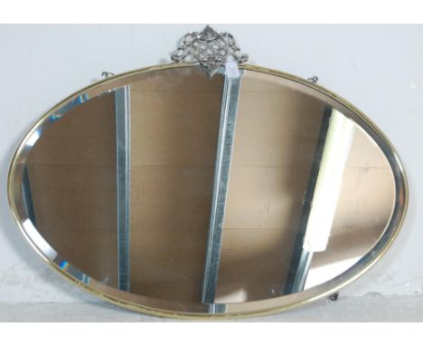 A vintage 20th century antique style brass framed mirror of oval form having a pierced armorial motif to the top. Measures 75