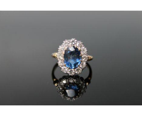 AN 18CT GOLD SAPPHIRE AND DIAMOND RING, the central oval claw set sapphire measures approx. 10 mm x 7 mm, surrounded by twelv