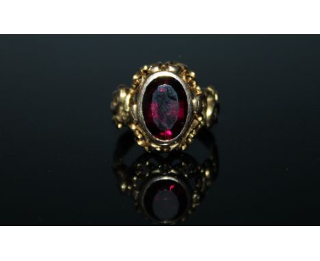 A FANCY SET AMETHYST RING, rub over set in pierced scrolling yellow metal the amethyst having faceted sides and being of appr