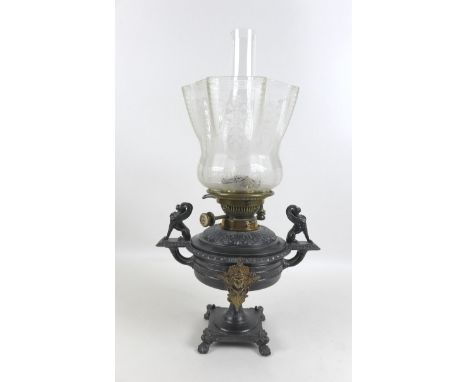 A Victorian cast metal paraffin lamp, with clear glass reservoir on a cast base, decorated in relief with winged handles, cle