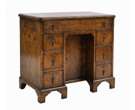 A George I crossbanded walnut kneehole desk the quarter veneered top with re-entrant corners over one long drawer and six sho