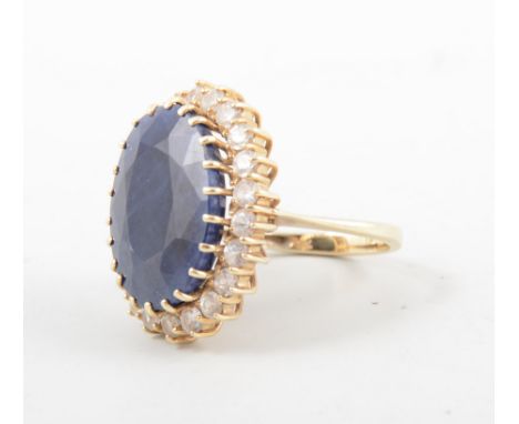 A large sapphire dress ring, the oval mixed cut stone, 18mm x 15mm claw set and surrounded by twenty-two synthetic white ston