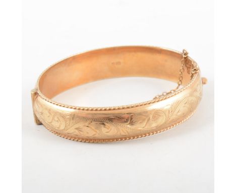 A 9 carat yellow gold hollow half hinged bangle in the Victorian style, scroll engraved pattern to front with a milled border