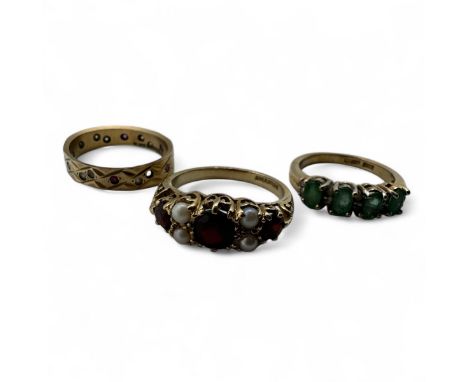 Three 9ct gold dress rings. To include a Victorian style 1970s garnet and seed pearl half hoop ring, size N 1/2; an emerald a