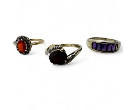 Three 9ct gold gem set dress rings. Featuring a fire opal and diamond cluster ring, size Q; a garnet and diamond set crossove