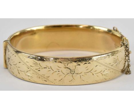 A 9ct gold metal core hinged bangle, the front with floral detail, the back plain, with safety chain, internal diameter 6.6cm