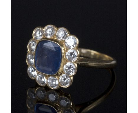 A sapphire cluster ring, the central cushion cut stone approximately 7.5mm x 7mm, surrounded by twelve paste stones to a yell