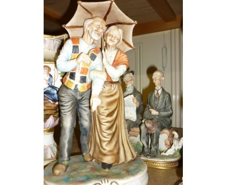 Two Capo di Monte figure groups, elderley lady and gentleman beneath an umbrella and two elderley gentlemen seated on a bench