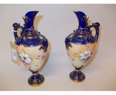Pair of Royal Worcester jug vases painted with panels of flowers on a blue and gilt ground (one a/f)