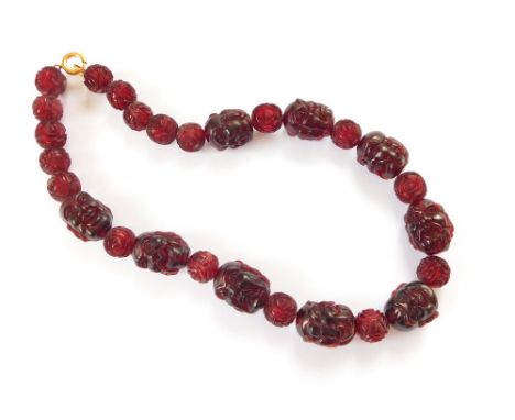 CHINESE CARVED BEADS. A necklace of Chinese wine-red beads, the large beads carved with a variety of faces of Immortals to ei