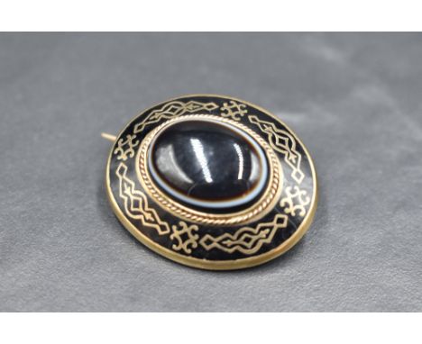 A Victorian gold and black enamel mourning brooch having a central bulls eye agate cabochon and glass locket en verso, approx