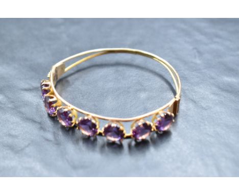 A yellow metal hinged bangle stamped 14 of open tubular form having seven inset amethysts, approx 14g gross