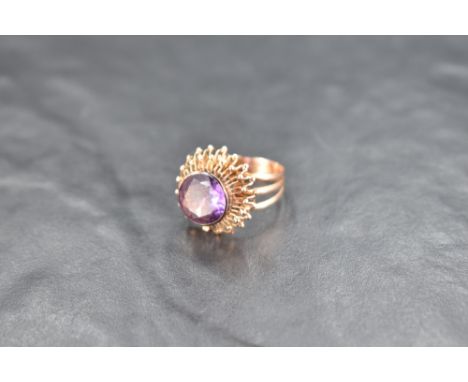 An amethyst solitaire ring having a facet cut circular stone in a collared mount on a raised star burst style setting on a ye