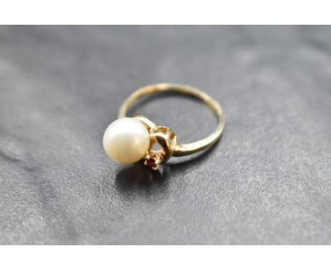 A cultured pearl ring with ruby chip set swirl mount on a yellow metal loop stamped 10K, size N &amp; approx 2.4g