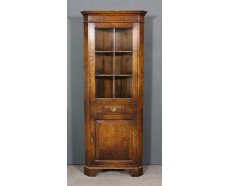 A modern oak corner cupboard by Manor Hall Furniture, the upper part with moulded cornice, fitted two shaped shelves enclosed