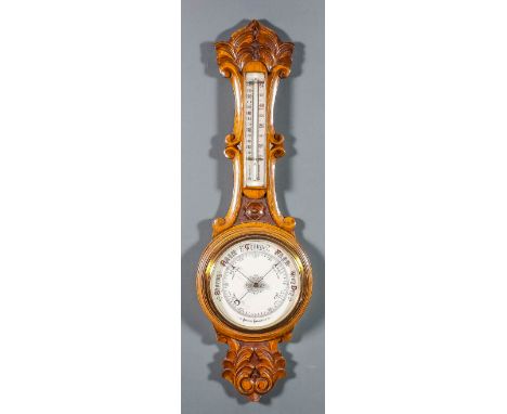 A late Victorian oak cased aneroid barometer and thermometer with 7.25ins diameter white dial, in wheel pattern case carved w