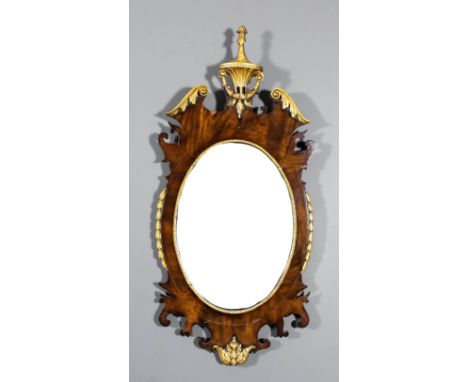 A mahogany framed and parcel gilt oval wall mirror, with bow front reeded and bellflower cresting, the frame of shaped outlin